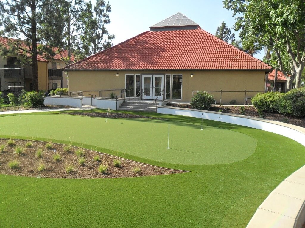 Backyard of a house with a well-maintained golf green. The area is dry, but the artificial turf provides a completely natural appearance.
