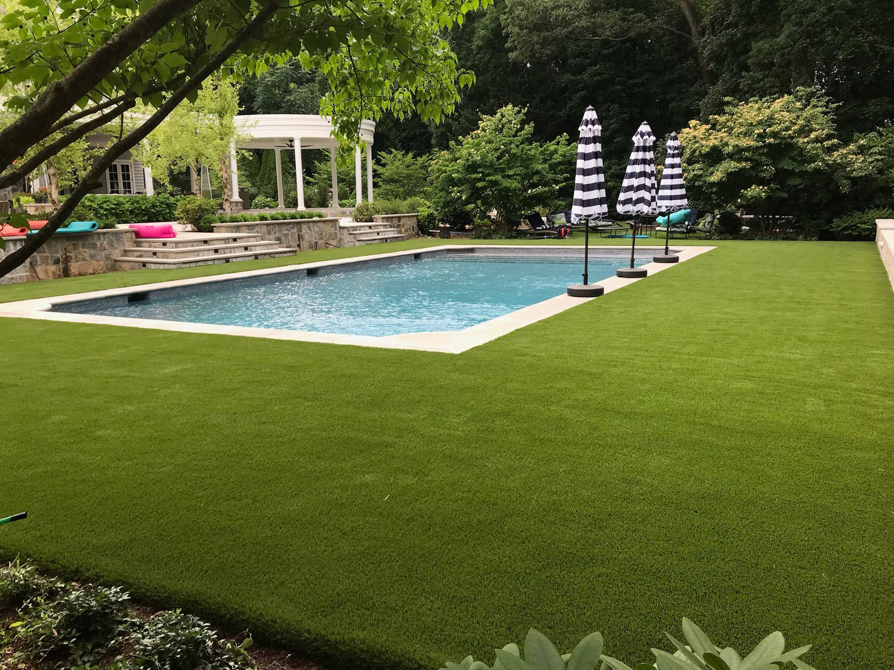 Clear-water swimming pool, area with artificial turf, and a tropical-looking garden.
