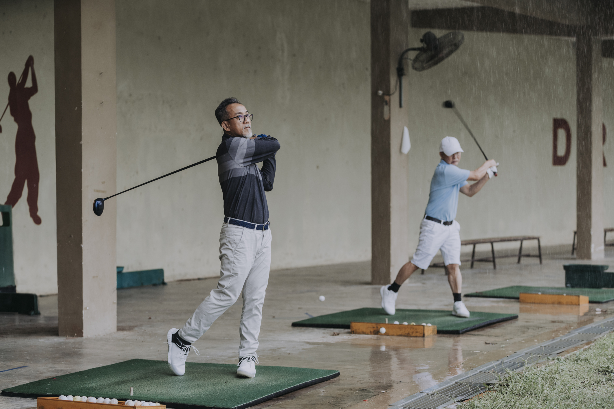 People practicing golf while it's raining outside.