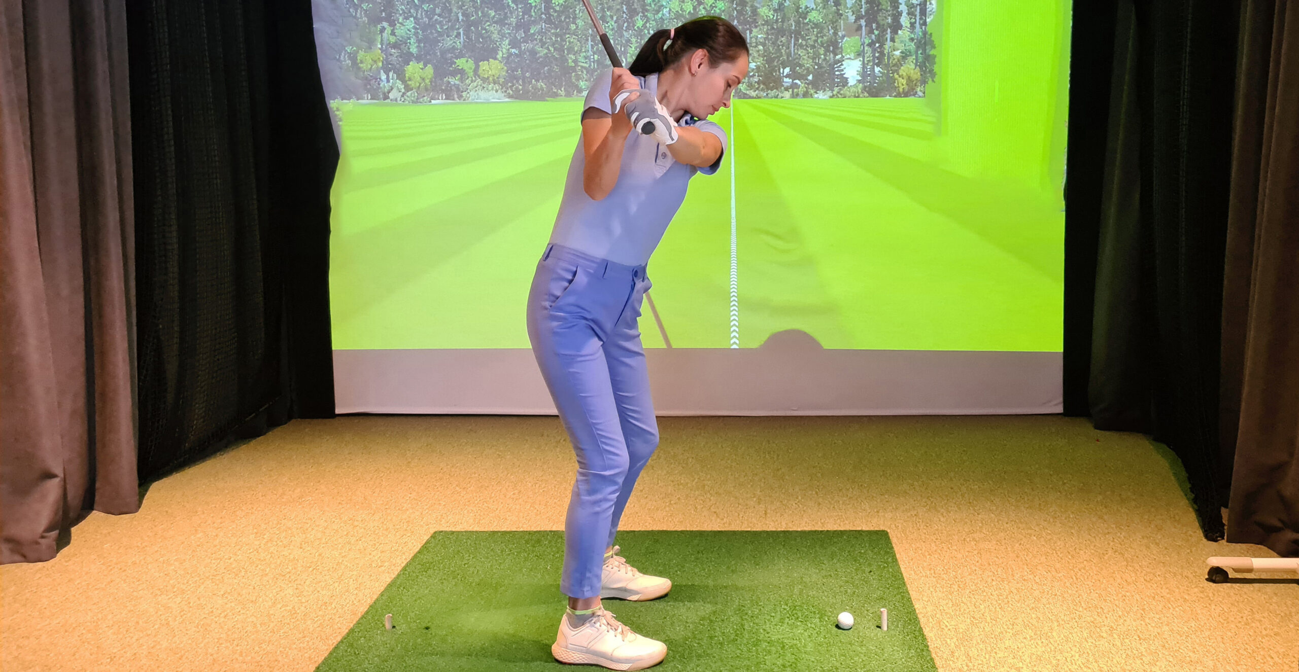 Woman playing golf on screen and golf simulator.