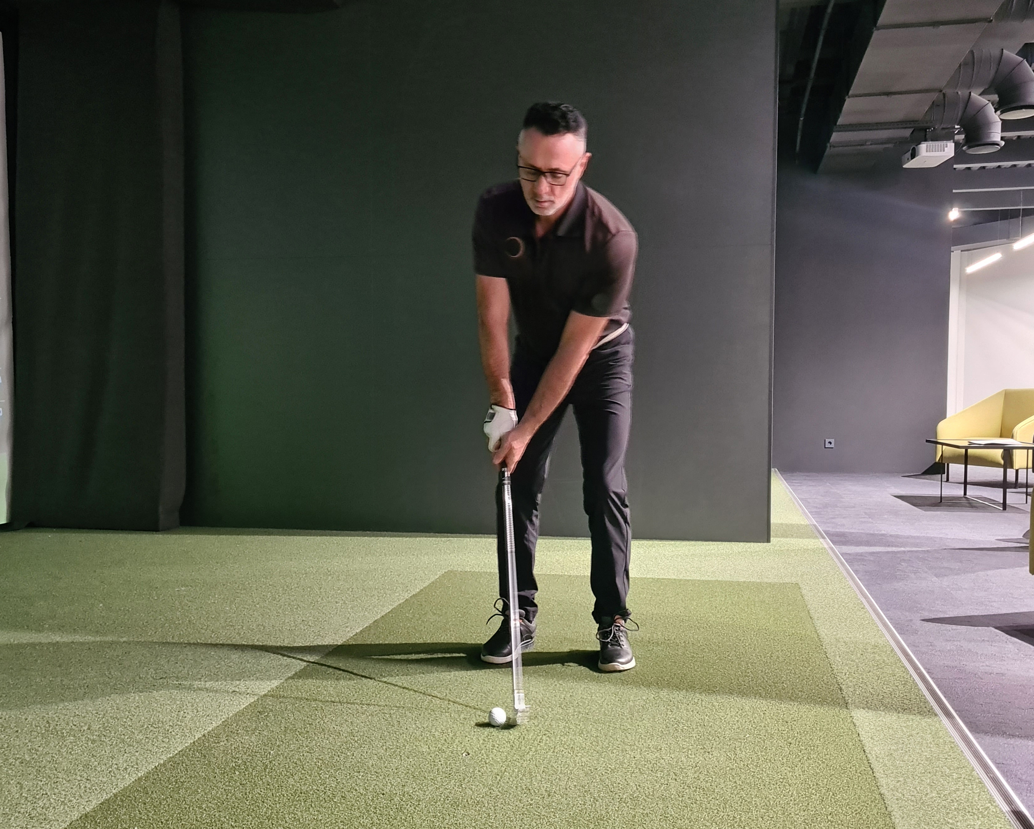 Golf indoor area for practice. A man is hitting the ball in virtual simulator.